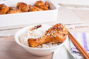 A bowl of rice and fried chicken in a sticky sweet sauce chicken drumstick, sprinkled with sesame...