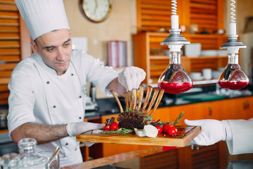 The cook passes the waiter the finished dish. rack of lamb.