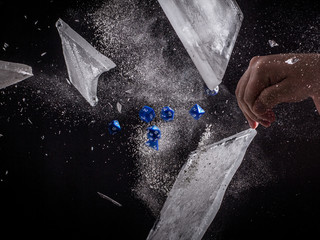 Blue Role Playing Dice Exploding through a Sheet of Ice - with a Caucasian Man's Hand to the Side Tossing the Dice and a Black Background