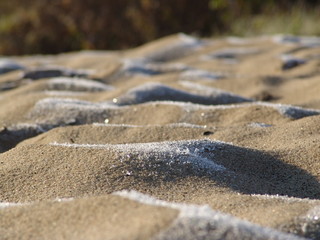Sand in the hoarfrost on the river bank. Snow on the sand dunes early in the morning.