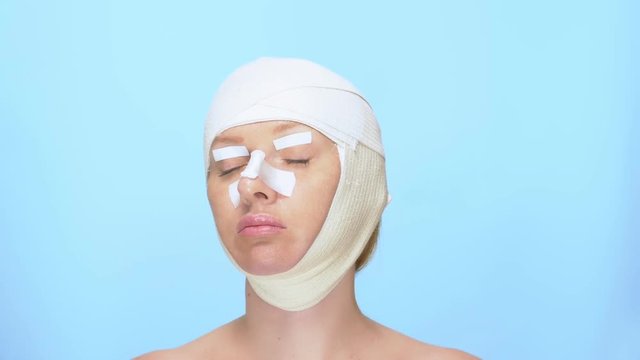 The concept of plastic surgery. rhinoplasty, blepharoplasty, face lift. Portrait of a woman with a bandage on his head, nose and eyes. on blue background