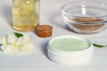 Jar of cream made from natural plant ingredients, oils and herbs, jasmine flowers on a white wooden background - preparation of organic cosmetics concept, close up