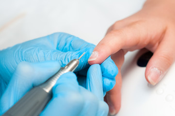 Woman use electric nail file drill in beauty salon. Perfect nails manicure process or operation in close up.