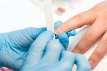 Closeup shot of a woman in a nail salon receiving a manicure by a beautician with nail file. Woman getting nail manicure. Beautician file nails to a customer.