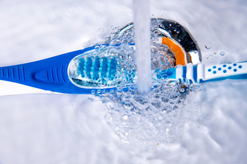tongue cleaner and toothbrush under running water in the bathroom