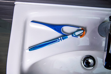 Tongue cleaner with toothbrush on the wash basin in the bathroom