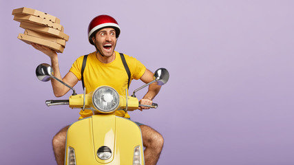 Scared emotional male courier shouts loudly, being on way to customer, late to bring order in time, holds pile of cardboard boxes of pizza, drives scooter, isolated on yellow background. Delivery
