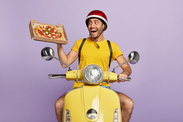 Fast food delivery concept. Happy busy courier or deliveryman shows fresh baked pizza on box, poses...