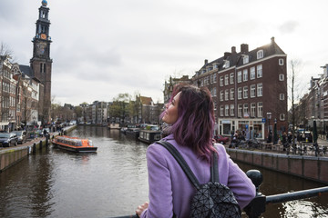 Fototapeta na wymiar Girl in the coat and backpack enjoying Amsterdam city. Young woman looking to the side on Amsterdam channel
