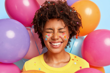 Overjoyed pleased woman with Afro hairstyle, smiles broadly, expresses positive emotions, has...