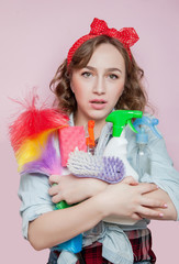 Beautiful young woman with pin-up make-up and hairstyle with cleaning tools on pink background © volody10