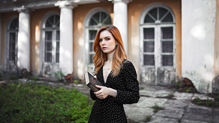 Red-haired girl stands alone in an abandoned park with a book in her hands