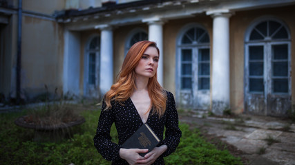 Red-haired girl stands alone in an abandoned park with a book in her hands