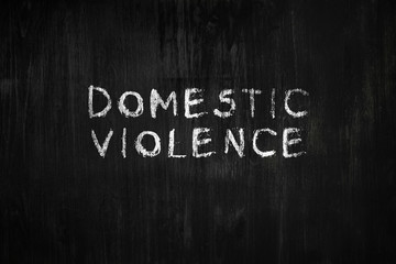 Domestic violence phrase handwritten on black wood background. Sign, concept of dealing with...