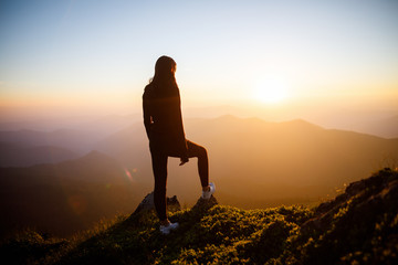 Girl on the background of mountain peaks. Woman hiking in mountains. Happy traveler standing on top of a mountain and enjoying sunset view