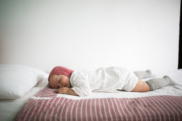Cute baby in crocheted cap sleeping on tummy, bed