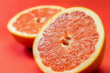 Grapefruit cut in half on vivid red background. Fruitarianism, vegetarian or vegan food: close-up view of fresh and ripe citrus fruit in bright colors