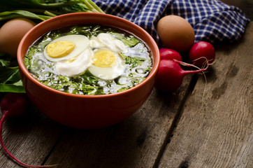 Green borscht with sorrel, spinach and potato, topped with boiled egg and sour cream on a vintage wooden table.