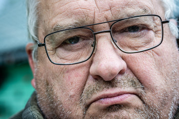 Brooding unshaven old grandfather in dirty glasses looks in front of him