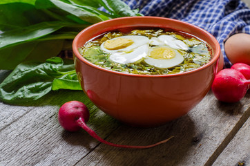 Green borscht with sorrel, spinach and potato, topped with boiled egg and sour cream on a vintage wooden table.