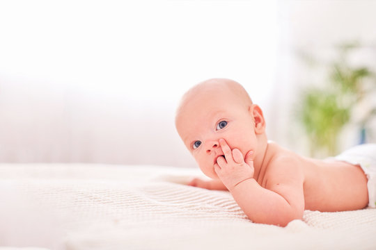 A Baby With A Hand In His Mouth. Teething In Children. Sucking Reflex. Hungry Little Baby. Lying On His Stomach On Their Own Holds Head. Sign, Symbol.