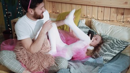Happy father and daughter have fun together play on bed laugh and smile of joy. Daddy and his little girl playing fairies at birthday party at home.