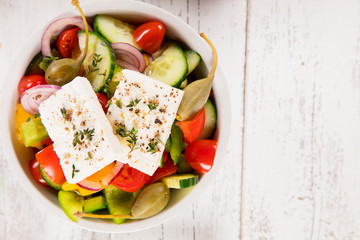 Greek salad with feta cheese, fresh vegetables and olives on old white wooden background, top view