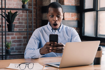 Young african business man looking at online content on his phone, WOW concept