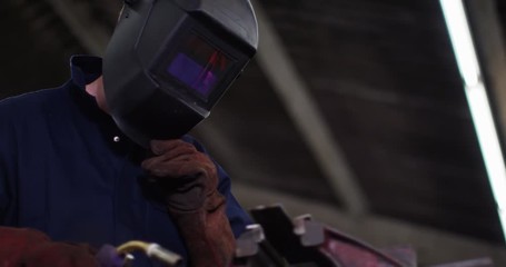 4K Metalworker in safety clothing closing visor to weld steel, with sparks flying. Slow motion