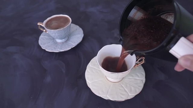 White coffee cup filled with Turkish coffee. Someone pouring traditional Turkish coffee. Two cofee cups on purple background