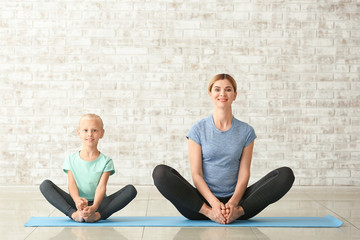 Mother with little girl doing yoga indoors