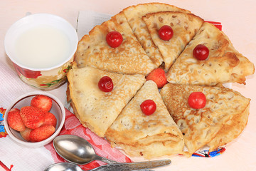 Delicious Russian pancakes with cherries and strawberries and a mug of milk on a bright table, top view, selective focus. Traditional Russian pancakes, natural food, jam and berries with milk.