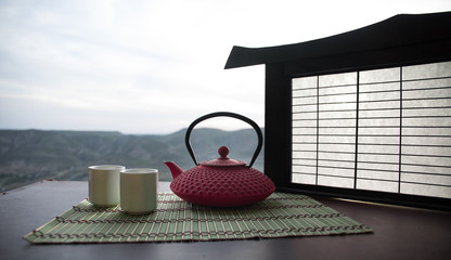 Fototapety  Koncepcja herbaty. Japońskiej kultury ceremonii parzenia herbaty wschodni napój. Czajnik i filiżanki na stole z liśćmi bambusa o zachodzie słońca