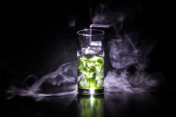 Cocktail glass splashing on dark toned smoky background or colorful cocktail in glass. Party club entertainment. Mixed light.