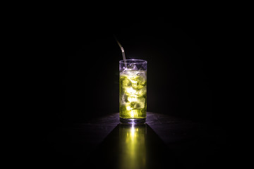 Cocktail glass splashing on dark toned smoky background or colorful cocktail in glass. Party club entertainment. Mixed light.