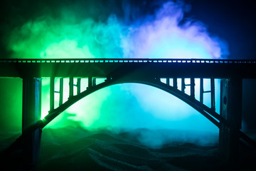 Artwork decoration. Silhouette of powerful metallic bridge at night with foggy backlight. Silhouette of person standing on bridge.