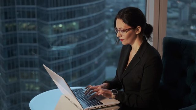 Portrait of a young woman working in an office near a large window. modern business woman working on a laptop in the evening.