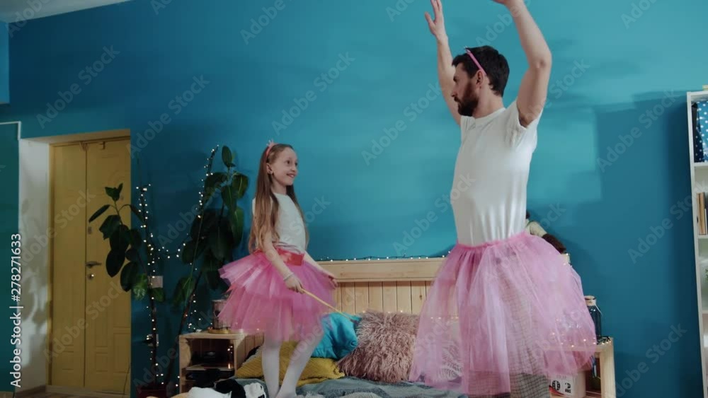 Wall mural Funny pretty fairy young daddy acting raising hands like ballerina in the room. Little sweet girl cheering and giving high five to her father. Amazing costume party at home.