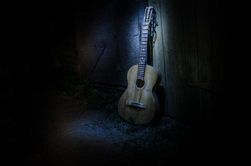 An wooden acoustic guitar is against a grunge textured wall. The room is dark with a spotlight for...