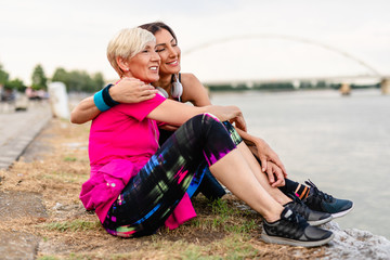 Happy mother and daughter enjoying together in beautiful sunset on the river