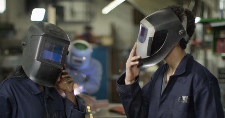 4K Young male & female welders in automotive industry smiling at camera. Slow motion.