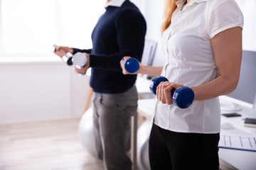 Businesspeople Exercising With Dumbbells In Office