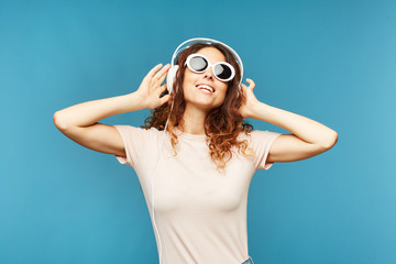 Happy young carefree female in headphones enjoying music at break in isolation over blue background