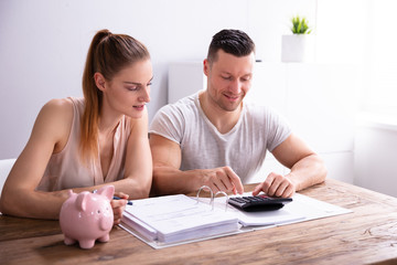 Obraz na płótnie Canvas Couple Calculating Bills Using Calculator Near Piggy Bank