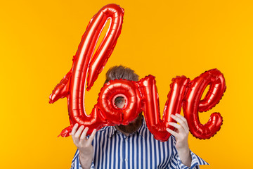 Indefinite man holding an inflatable love inscription in his hands on a yellow background. The...