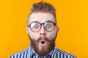 Young man with a mustache and beard rounded his mouth in surprise against a yellow background....