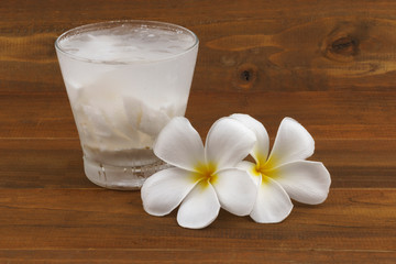 Fototapeta na wymiar Fresh coconut juice in glass and flower on wooden background