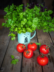 Vegetable set on a wooden plank table. Red tomatoes and a bunch of parsley in a ceramic turquoise mug, vertical shot