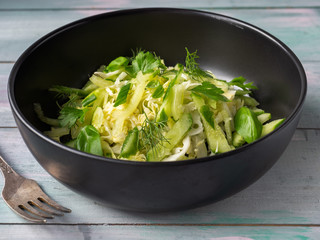 Cabbage salad with cucumbers and herbs in a deep black plate