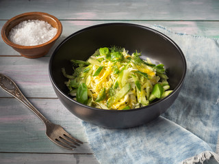 Cabbage salad with cucumbers and herbs in a deep black plate on a turquoise wooden tray, salt in a clay salt shaker